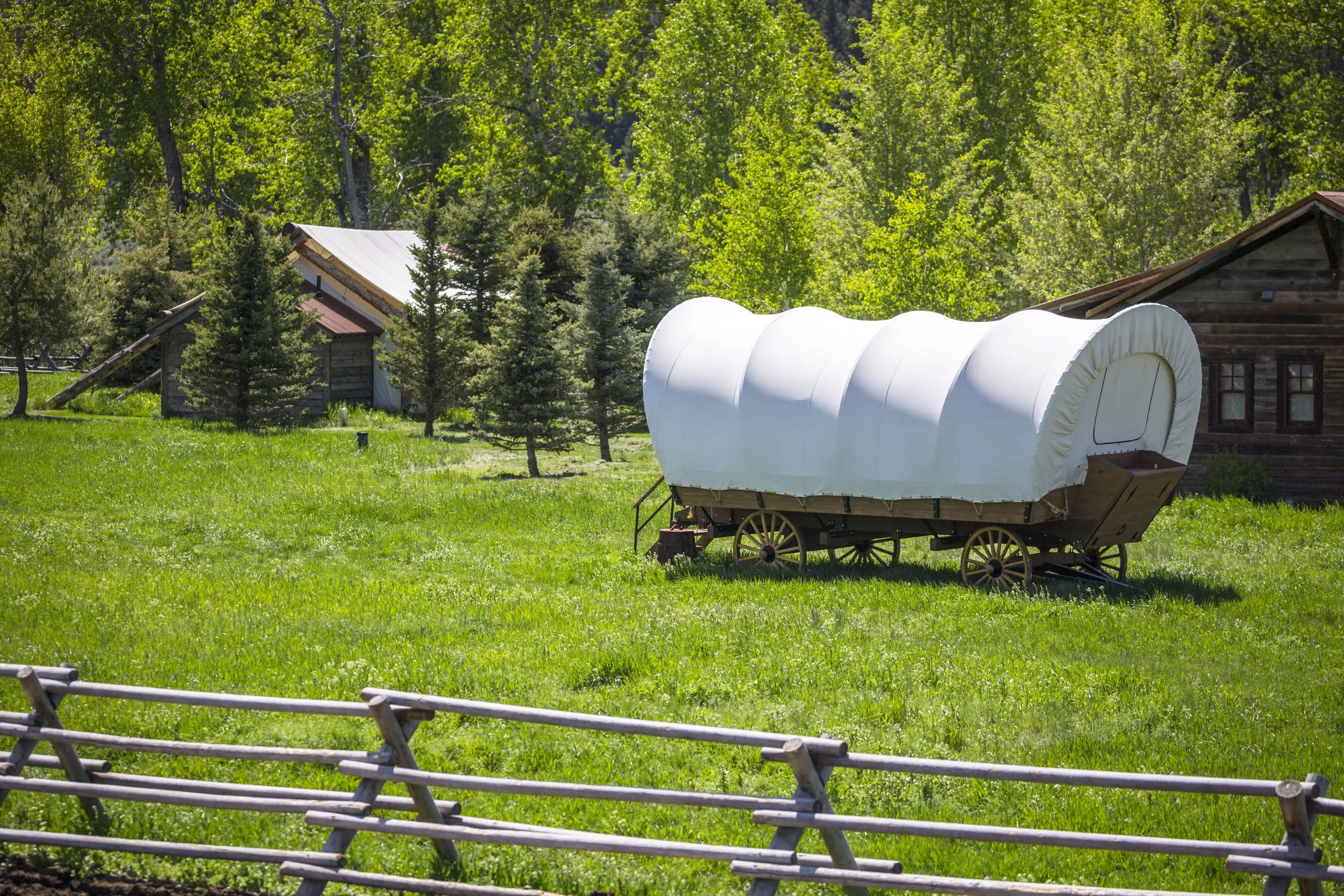 Covered wagon out in the field located next to two cabins and a fence