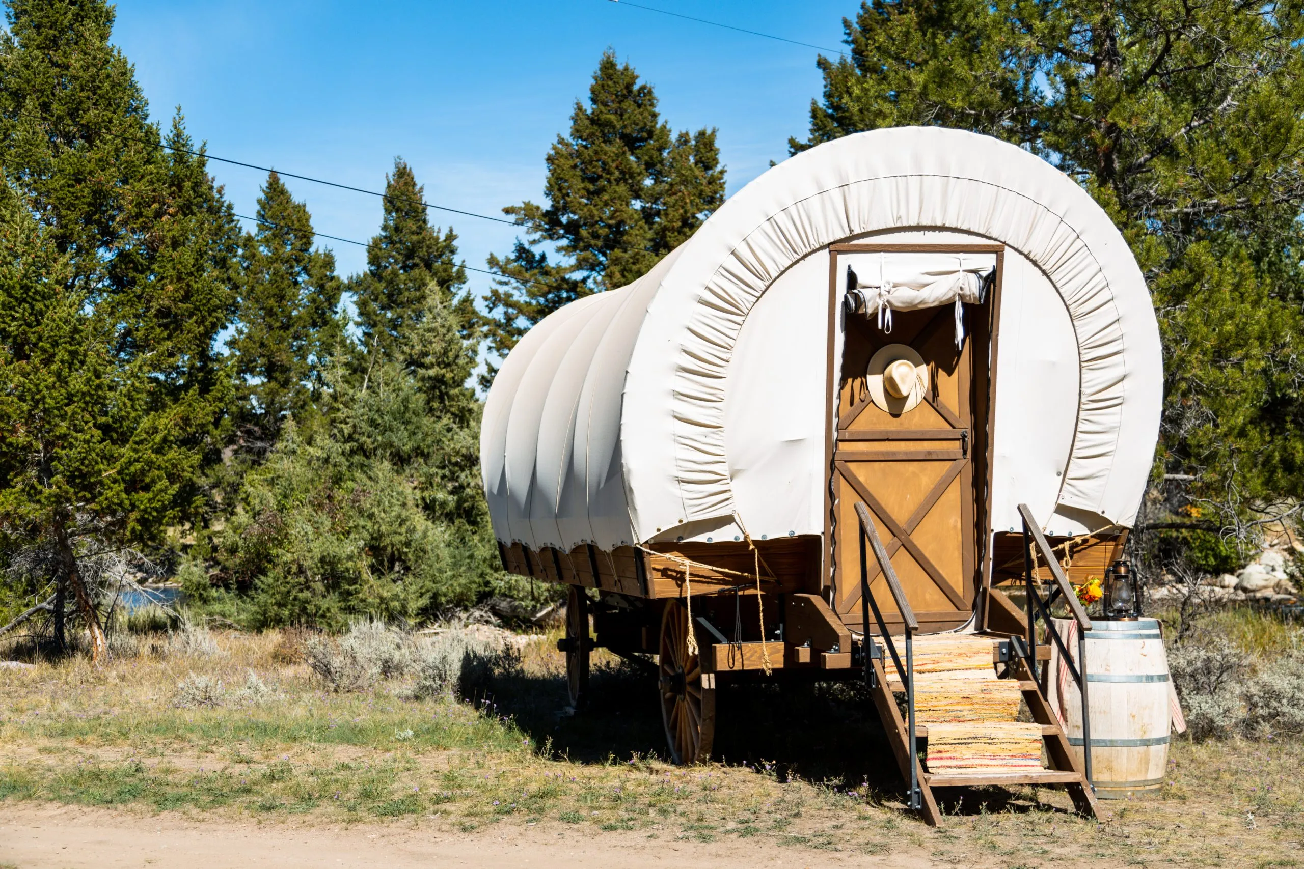 A wagon tent with stairs leading up to the door, cowboy hat hanging on the door outside