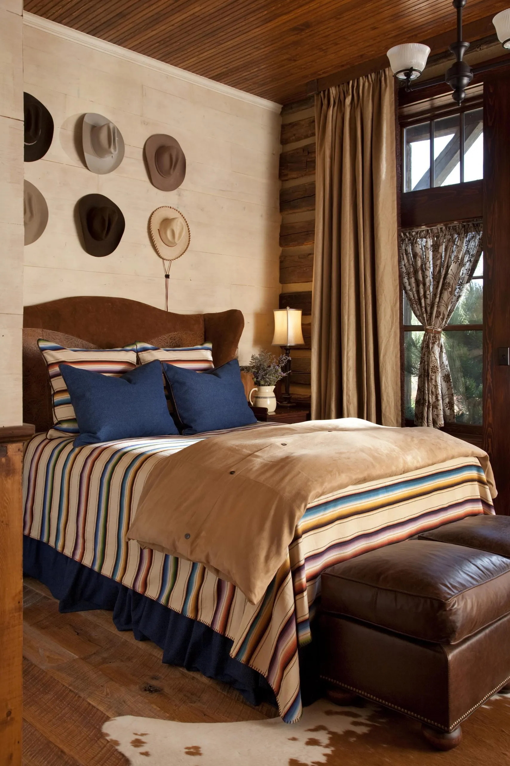 Bed with striped duvet and pillows with six cowboy hats mounted on the wall above the headboard