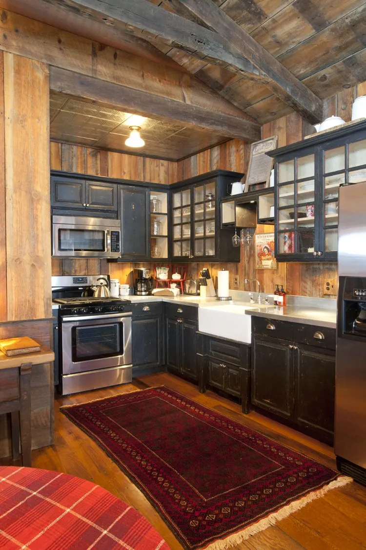 A kitchen inside a cabin with dark cabinets and a red rug
