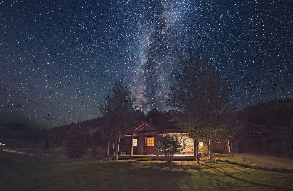 A ranch building with the lights on under a starry sky