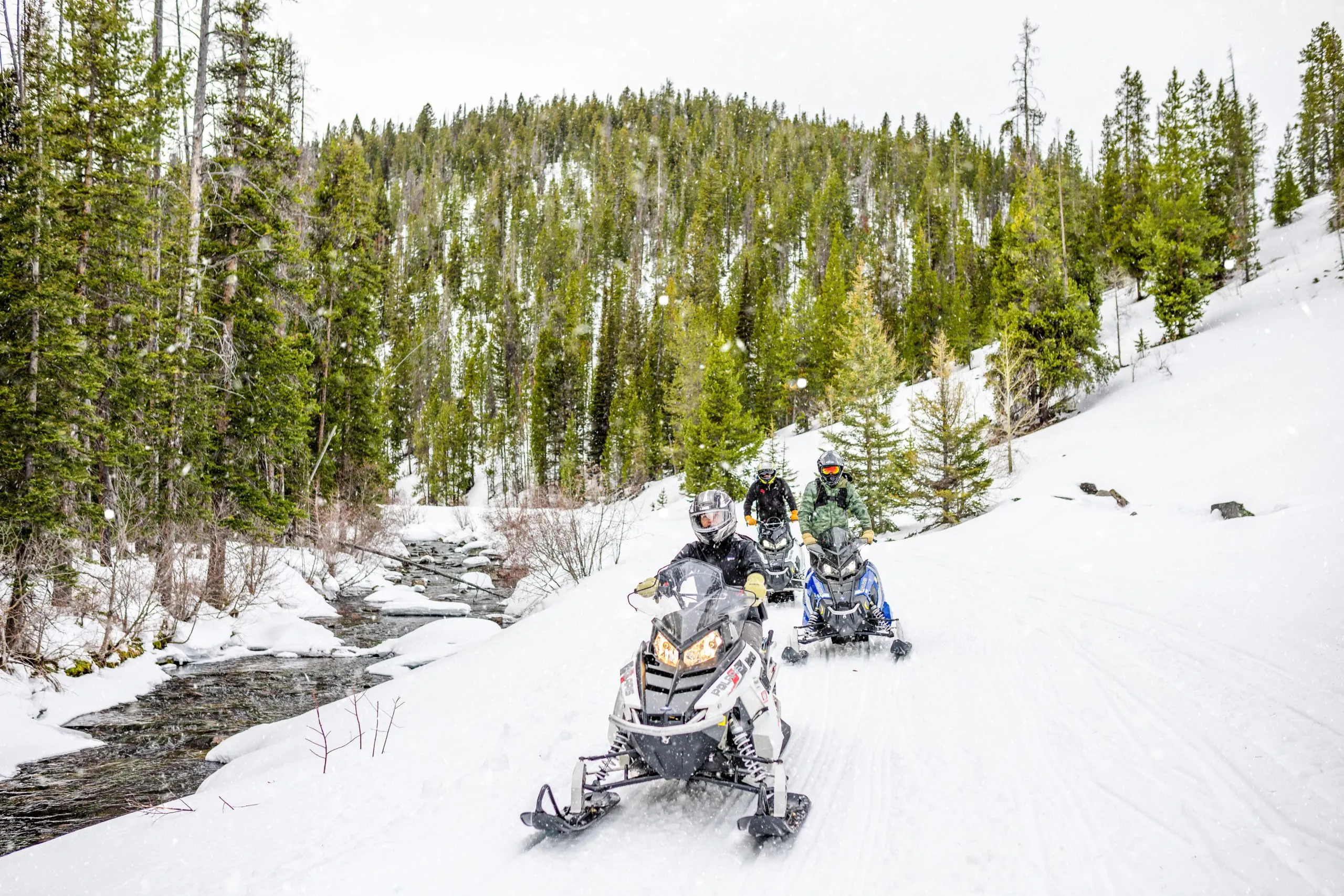 A group of snowmobilers riding next to a small creek