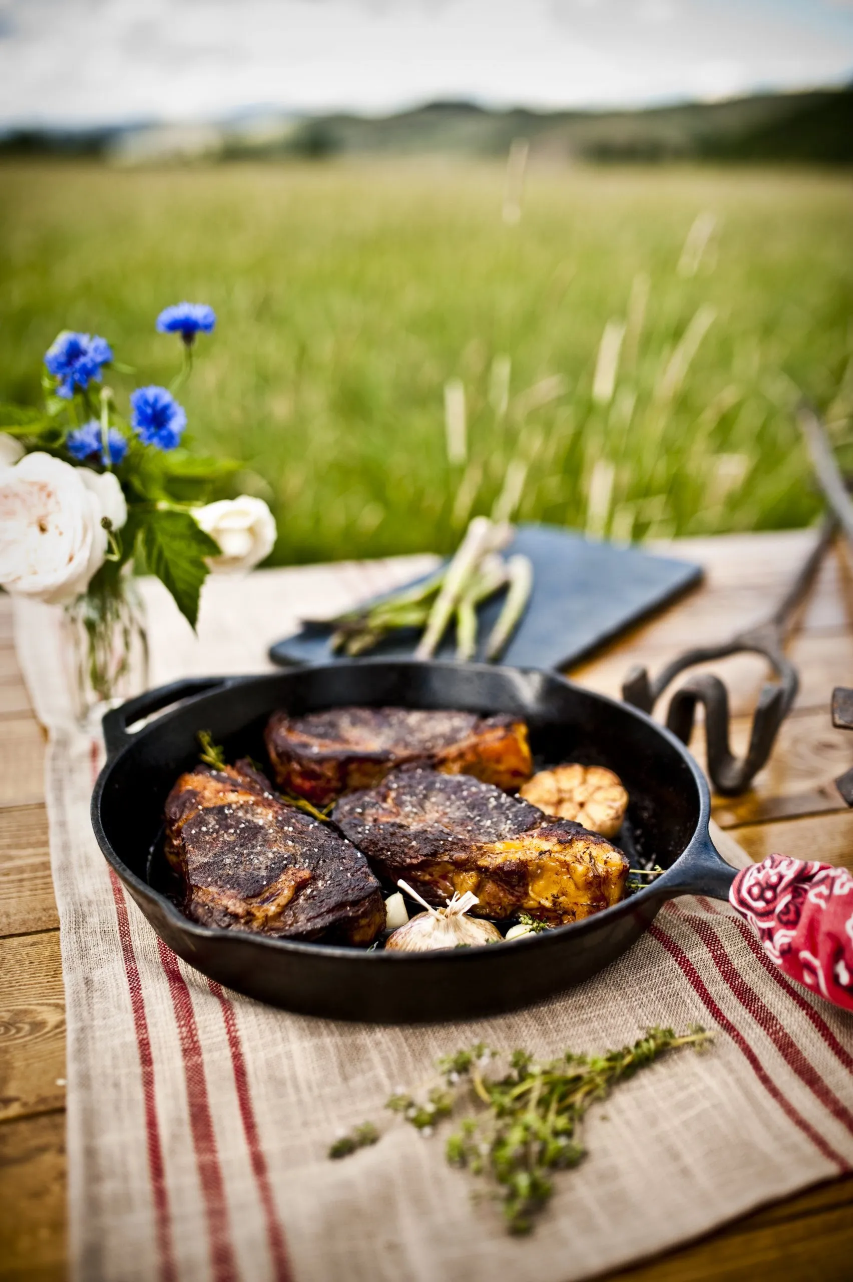 Three cooked steaks in an iron skillet on a wooden table outside