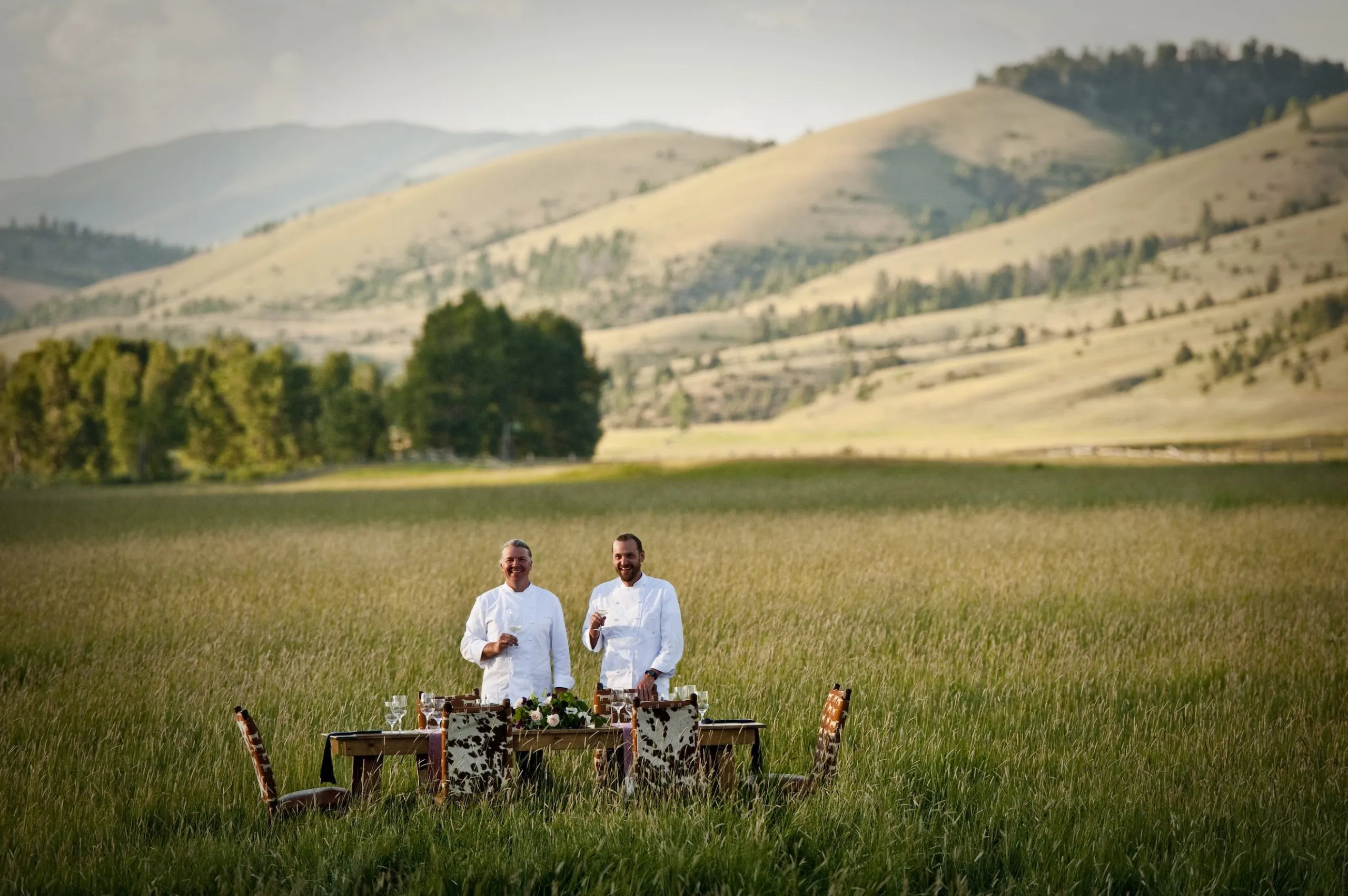 Two chefs stand at a dining table in an open field