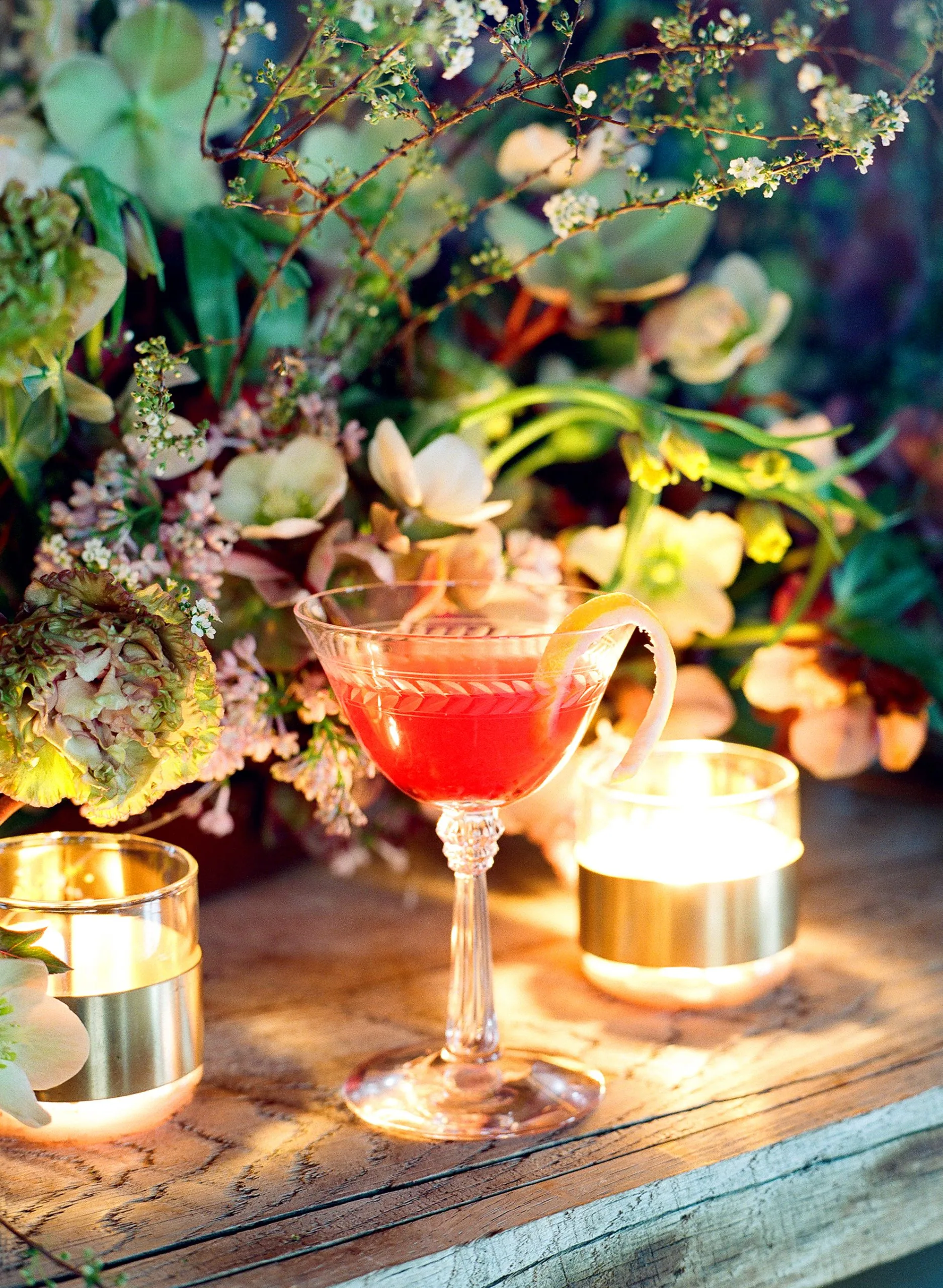 A cocktail on a table in front of a flower arrangement
