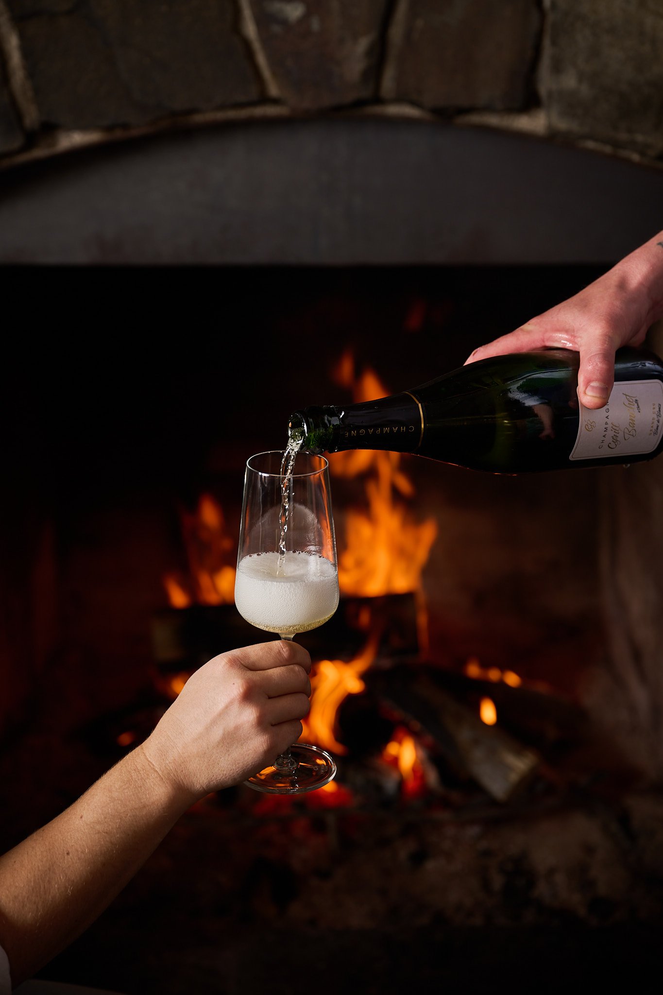 Champagne being poured into a glass beside a fireplace