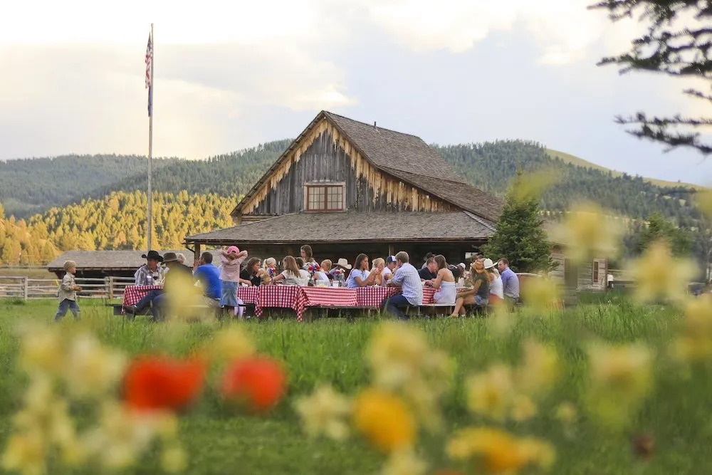 People eat at outdoor picnic tables in front of a barn building