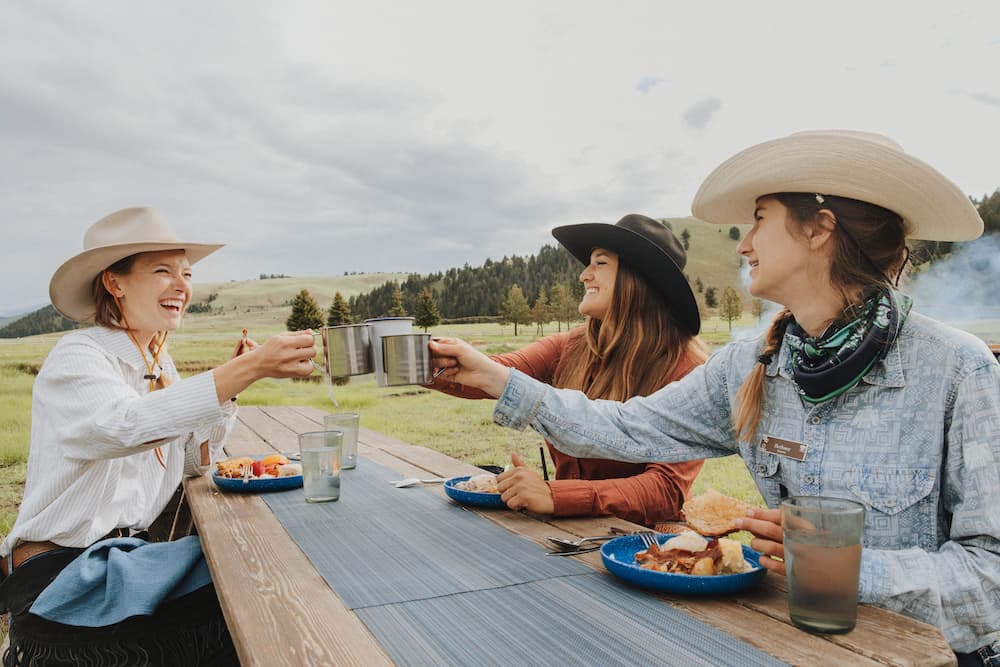 three people raising their cups while sitting at a table outside