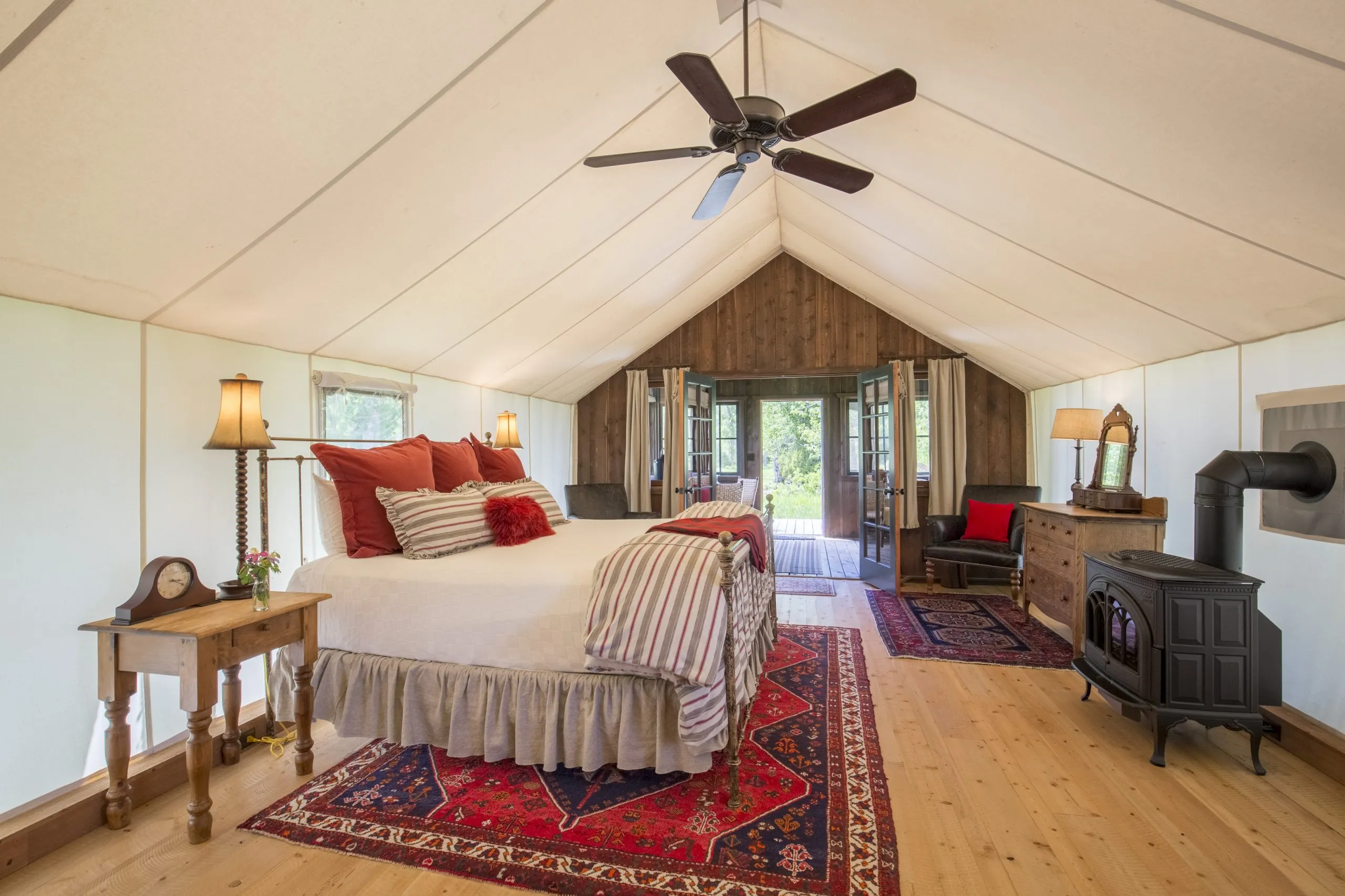 queen bed with rug underneath, ceiling fan above all inside a large tent