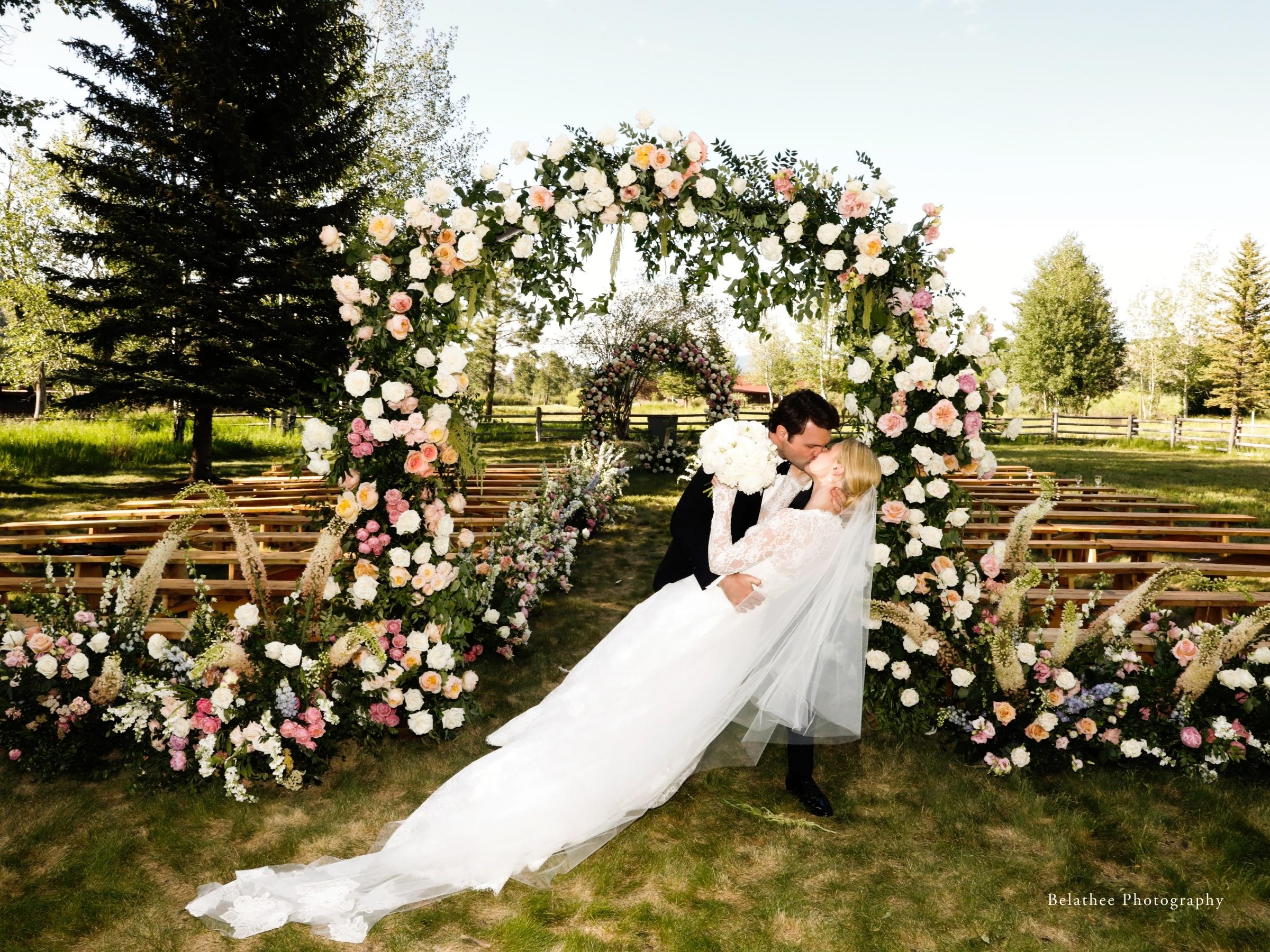 Wedding couple during first kiss under floral arch on River Lawn
